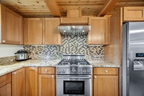 Una cocina con gabinetes de madera, estufa a gas, horno y refrigerador de acero inoxidable.