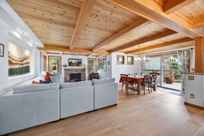 A spacious living area with a large sofa, a fireplace, wooden beams, and a dining table with chairs.