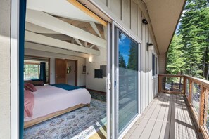 Un dormitorio con una cama grande, un ventanal corredero que da a un balcón y vistas a árboles.