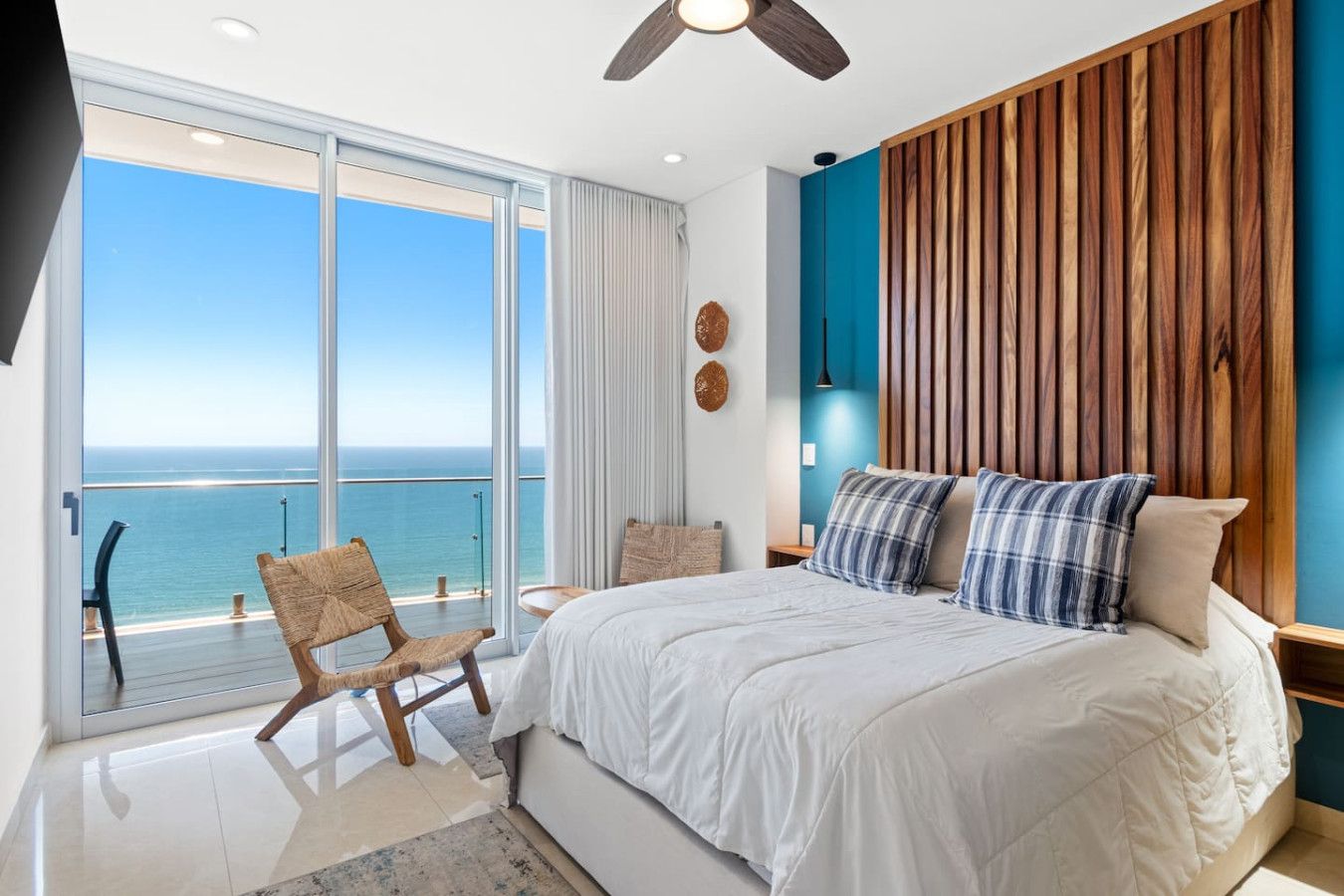 A bedroom with a large bed, a wooden headboard, a view of the ocean, and a balcony with a chair.