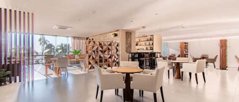 A spacious, modern dining area with a central round table, surrounded by chairs, and a large bookshelf in the background.