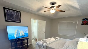 A bedroom with a bed, a ceiling fan, a TV, and a window with blinds. - The Good Life Place in Smyrna (Smyrna)