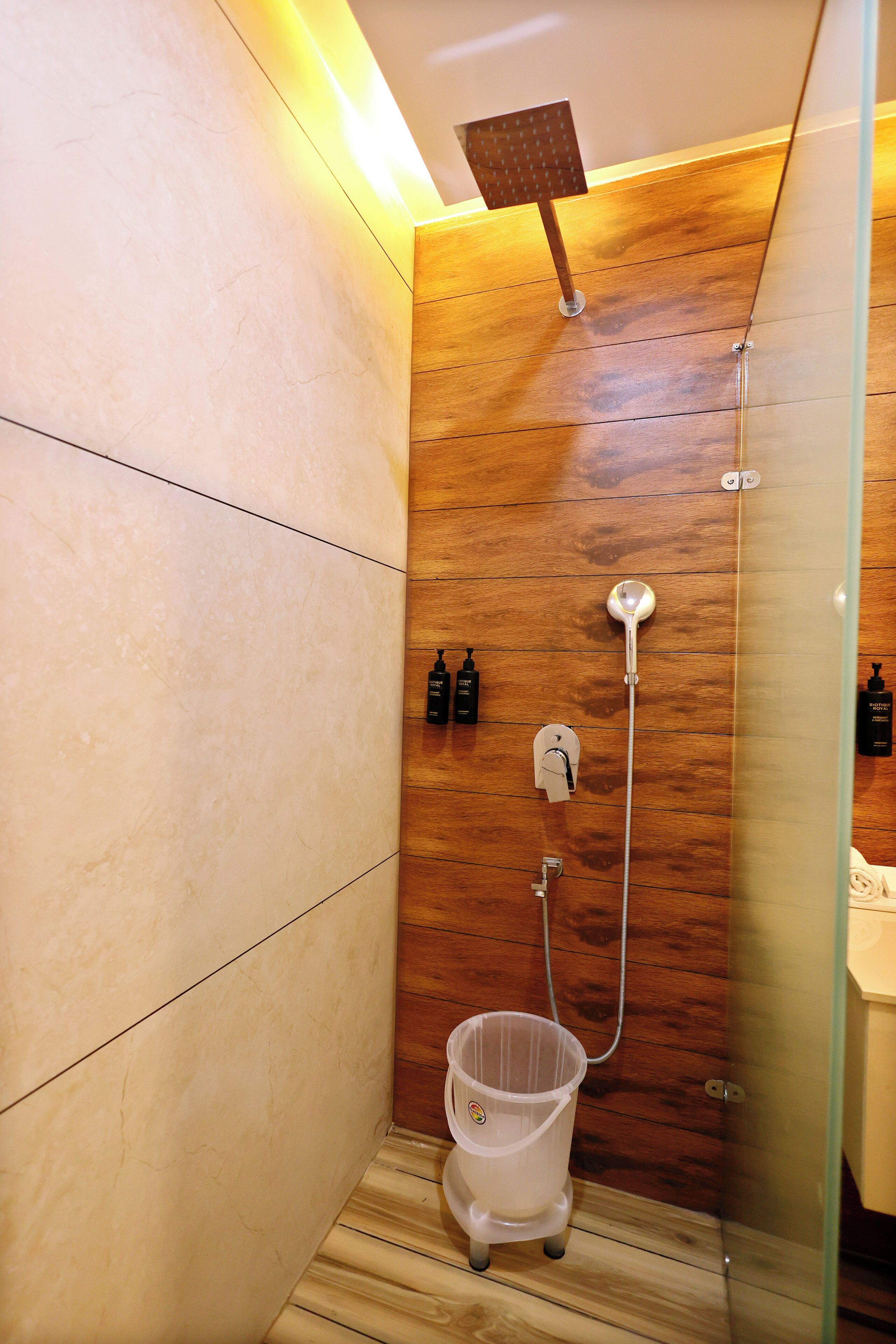 A modern shower with a wooden panel wall, a glass partition, and a white floor.