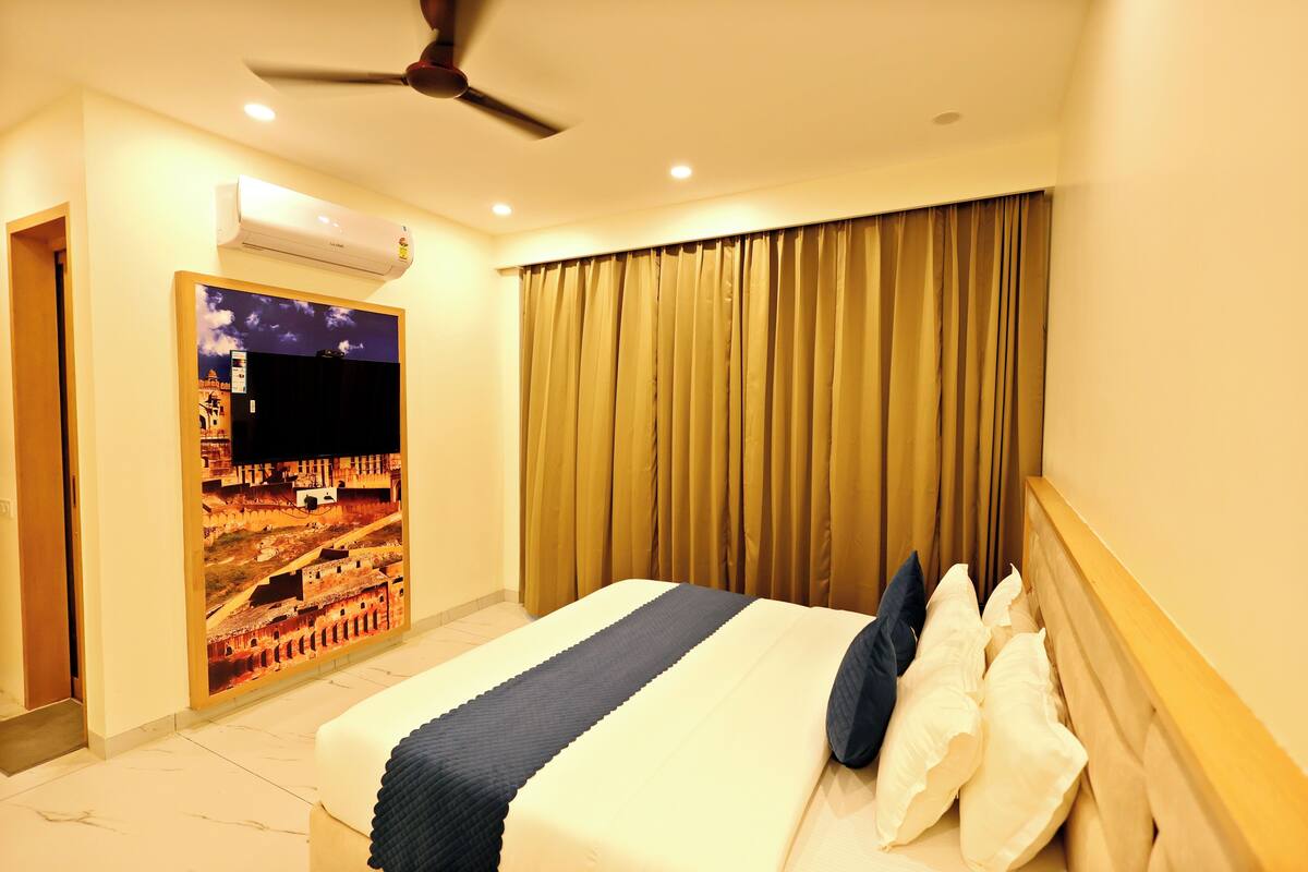 Habitación de hotel con cama, ventilador de techo, aire acondicionado, televisor de pared y cortina.