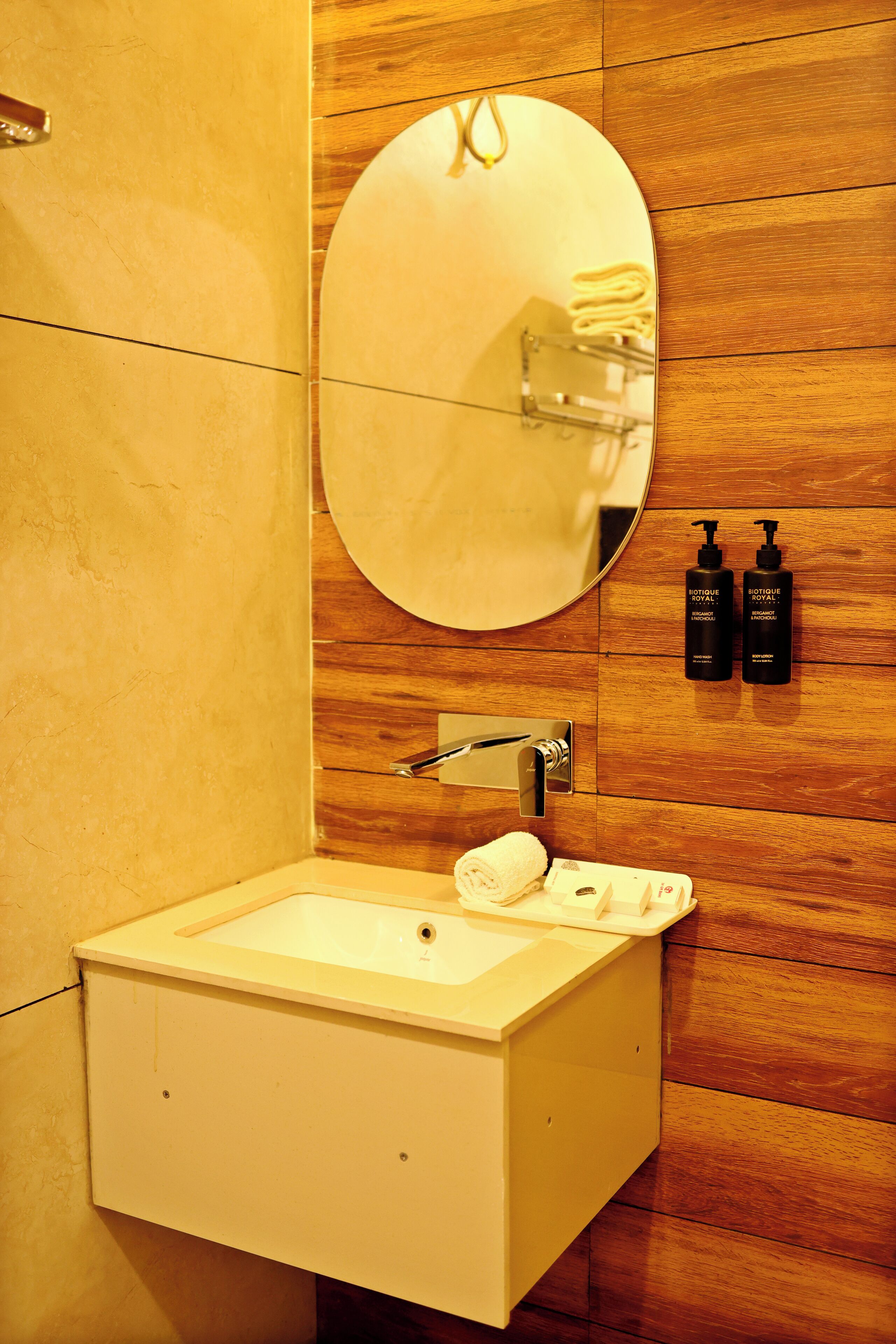Un baño con un lavamanos blanco, un espejo redondo y dos botellas de jabón de manos Biotique Royal.