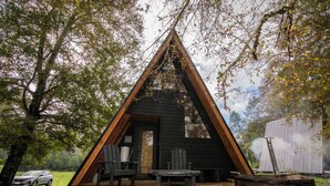 Une cabane en bois de forme triangulaire, dotée d’une terrasse, de meubles de jardin et d’un bain à remous extérieur.