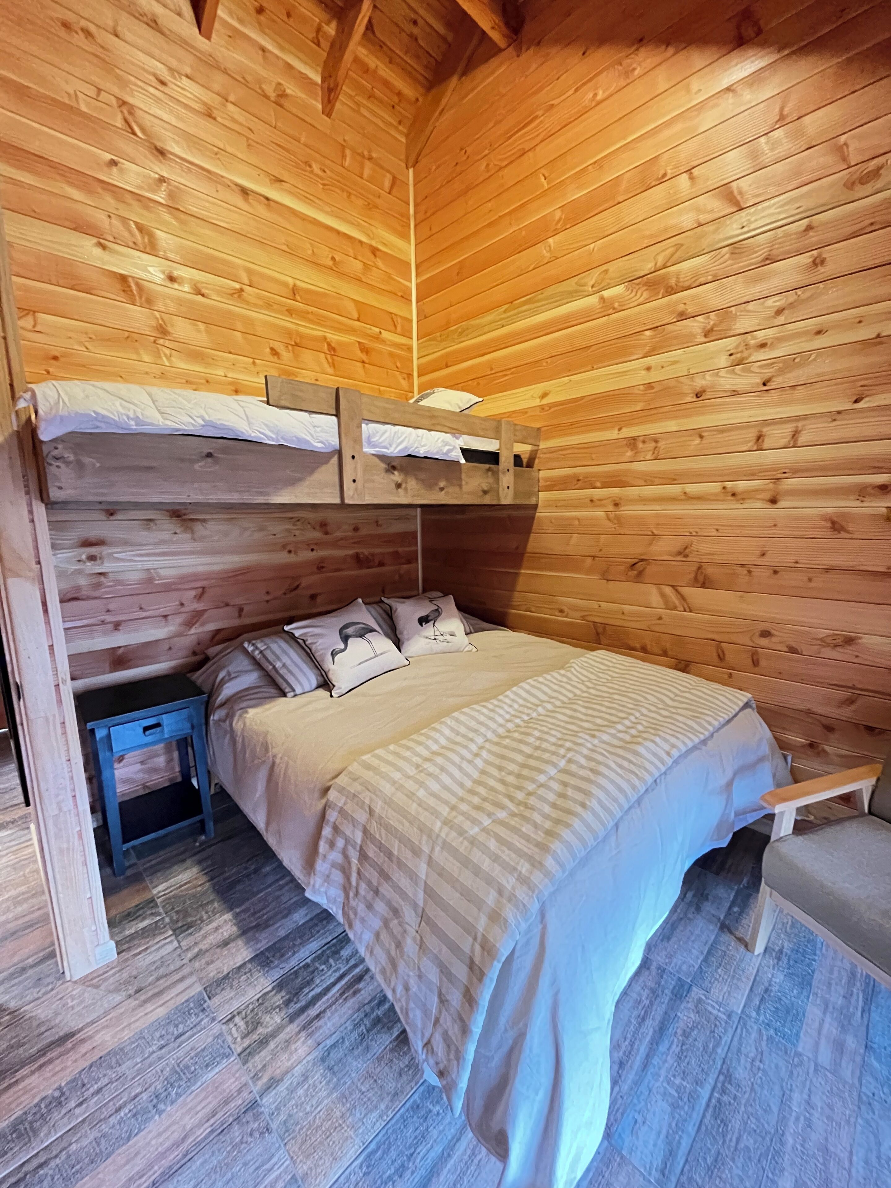 A wooden cabin room with a bunk bed, a small bedside table, and a bench.