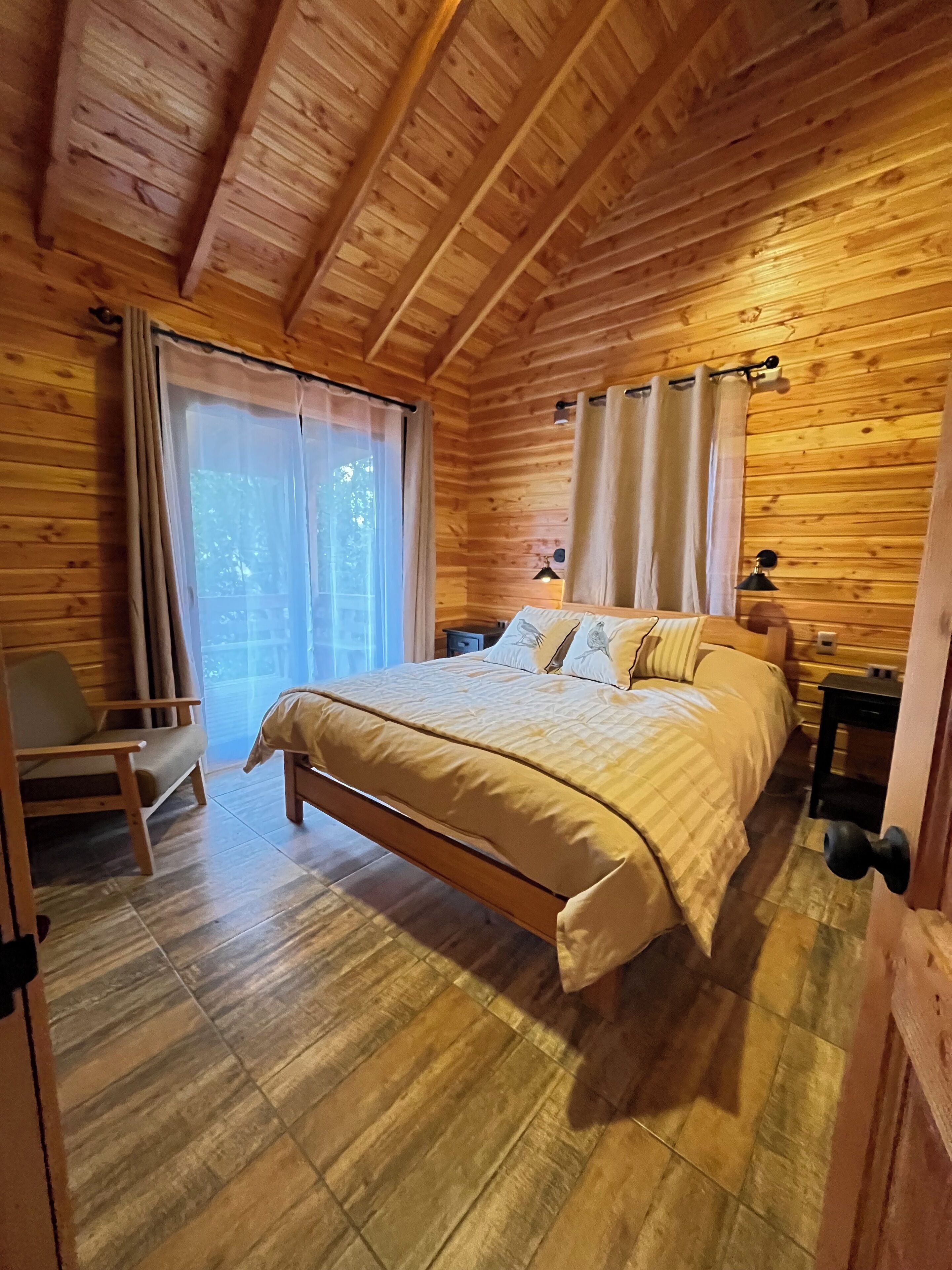 A wooden cabin bedroom with a bed, a chair, and a nightstand.