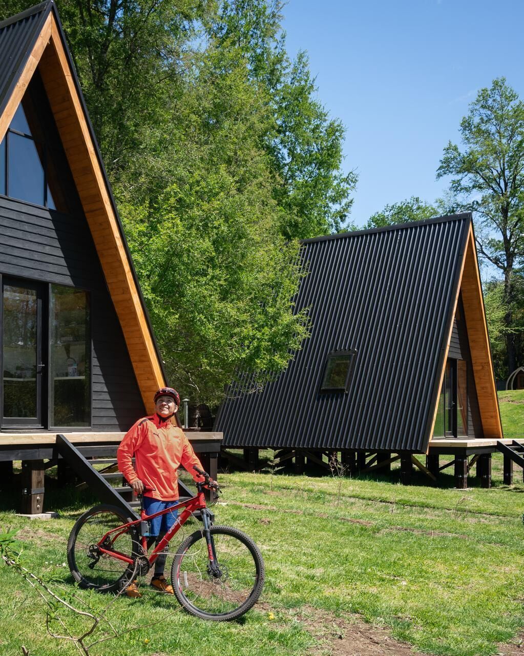 A person standing next to a red bicycle in front of a modern building with a sloped roof and wooden accents.