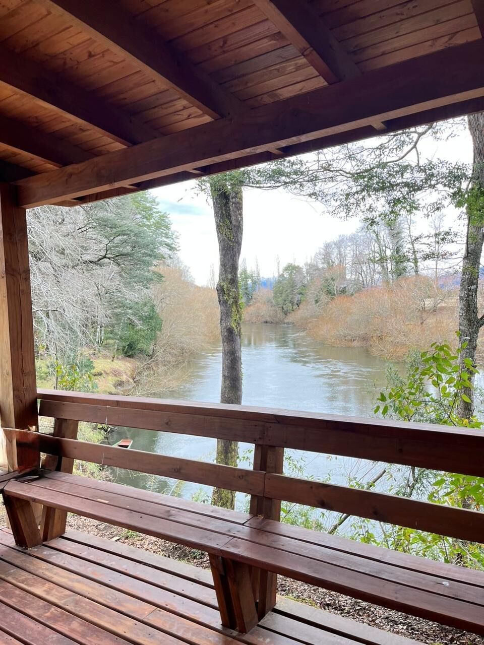 Um deck de madeira com um banco, de frente para um rio cercado por árvores.