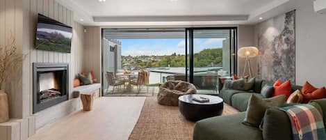 A modern living room with a fireplace, a large sofa set, a dining area, and a view of the city through large windows.