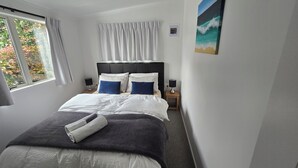 A neatly arranged bedroom with a bed, two bedside tables, and a window with curtains. - Orewa Kiwi Cabins - Kereru Cabin (Orewa)