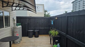 A patio area with a black fence, a table, two trash bins, and a potted plant. - Orewa Kiwi Cabins - Kereru Cabin (Orewa)