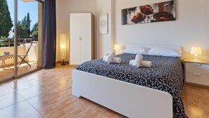 A bedroom with a bed, two bedside lamps, a painting, a wardrobe, and a balcony with a table and chairs.