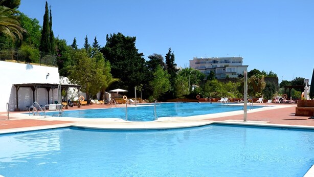 A swimming pool with a tiled deck, lounge chairs, and a building in the background.