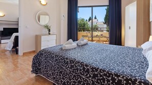 A modern bedroom with a large bed, a dresser, a TV, and a balcony with a view of the city.