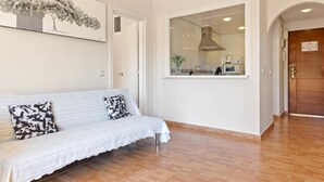 A modern living room with a white sofa, a large window, and a view of the kitchen.
