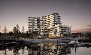 A multi-story hotel with balconies, a marina with boats, and a reflection in the water. - Crowne Plaza Shell Cove Marina (Wollongong)