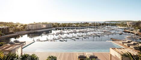 A marina with numerous boats docked, a large swimming pool, and lounge areas with sunbeds.