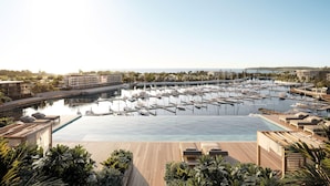 A marina with numerous boats docked, a large swimming pool, and lounge areas with sunbeds.