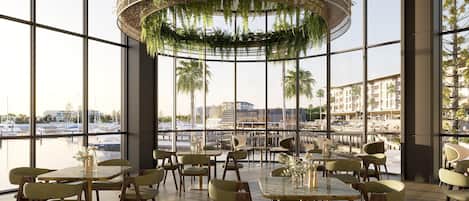 A spacious indoor dining area with large windows, modern furniture, and a hanging plant chandelier.