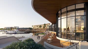 A waterfront restaurant with outdoor seating overlooking a marina, featuring a modern architectural design with large glass windows and wooden deck.