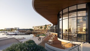A waterfront restaurant with outdoor seating overlooking a marina, featuring a modern architectural design with large glass windows and wooden deck. - Crowne Plaza Shell Cove Marina (Wollongong)