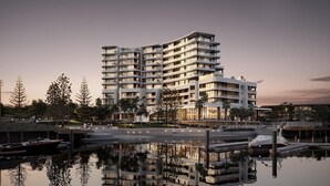 A multi-story hotel with balconies, a marina with boats, and a reflection in the water.