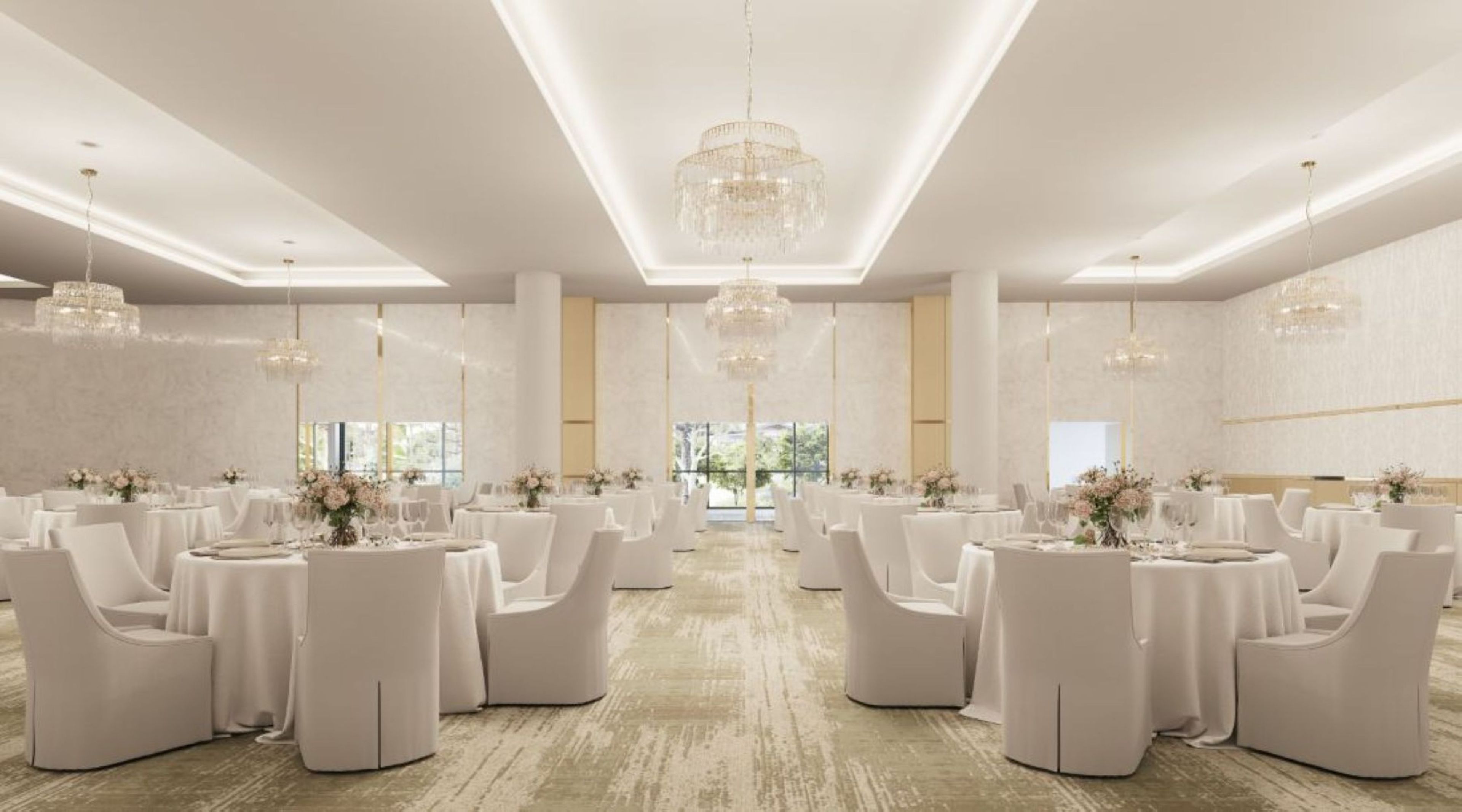 A spacious banquet hall with round tables and white chairs, large chandeliers, and a view of greenery outside.