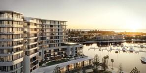 A modern multi-story hotel with balconies, a marina with boats, and a sunset view. - Crowne Plaza Shell Cove Marina (Wollongong)