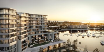 A modern multi-story hotel with balconies, a marina with boats, and a sunset view.
