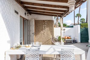 An outdoor patio with a white table set for dining, surrounded by white chairs, a decorative wall, and a hanging light fixture.