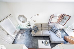 Uma sala de estar moderna com um sofá modular cinza, uma mesa de centro de vidro, um espelho redondo e um abajur.