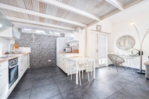 Una cocina moderna con armarios blancos, un salpicadero de piedra y un comedor con mesa y sillas blancas.