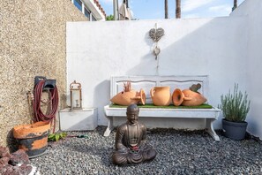 Una estatua de Buda, un banco blanco con cerámica y una planta en maceta en un patio.