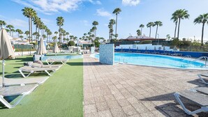 Zona de piscina con tumbonas, palmeras y cielo despejado.