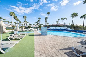 Zona de piscina con tumbonas, palmeras y cielo despejado.