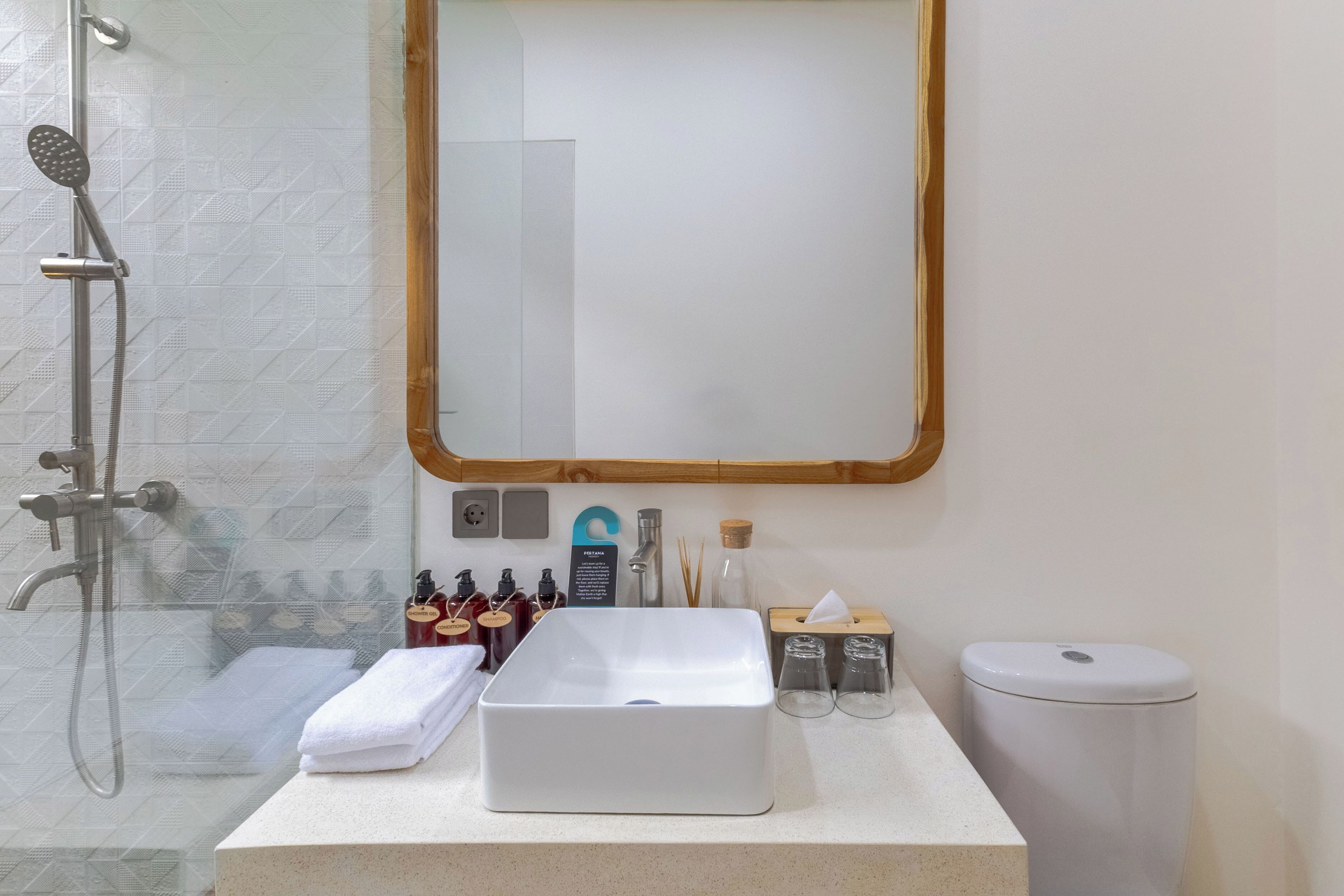 Een badkamer met een witte wastafel, een spiegel, een douche en toiletartikelen.