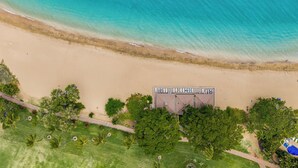 Vista aérea de una propiedad frente a la playa con zona de piscina, un paseo pavimentado y abundante vegetación.