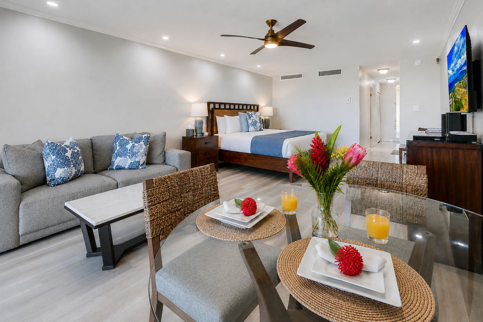 A modern hotel room with a bed, sofa, dining table, chairs, and a TV.