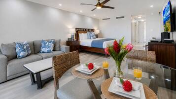 A modern hotel room with a bed, sofa, dining table, chairs, and a TV.