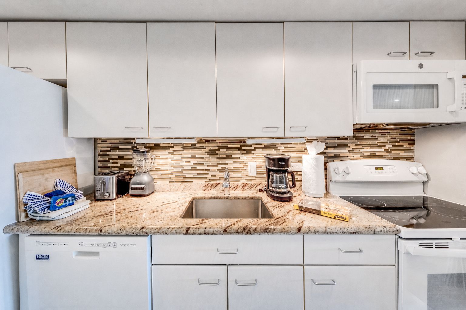 A modern kitchen with white cabinets, a granite countertop, a coffee maker, a toaster, and a microwave.