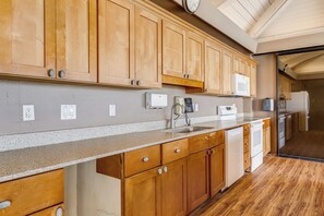 A kitchen with wooden cabinets, a granite countertop, a built-in microwave, and a dishwasher. - Kāʻanapali Ocean View Condo with Beachfront Cabana for Guests (Lahaina)