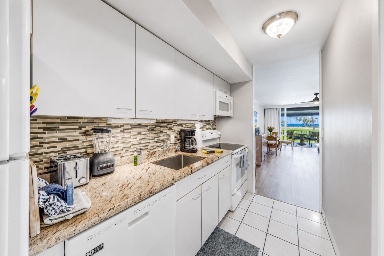 A modern kitchen with white cabinets, a granite countertop, and a view of the outdoor patio.
