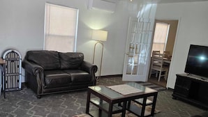 A living room with a dark leather sofa, a glass coffee table, a ceiling fan, and a television. - "Breaking Bad !"  Neighborhood -3-bedroom house  Albuquerque with WiFi, AC (Albuquerque)