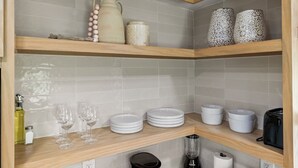 A kitchen with three wooden shelves, each holding various kitchenware and items.