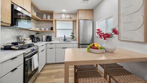 A modern kitchen with wooden cabinets, a stainless steel refrigerator, and a dining table with a vase of flowers.