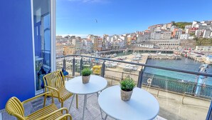 A balcony with yellow chairs and white tables, overlooking a harbor with boats and buildings.