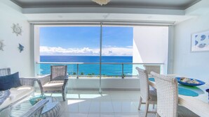 A balcony with wicker furniture, a glass railing, and a view of the ocean.