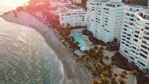 A coastal hotel with a pool, beach, and palm trees.